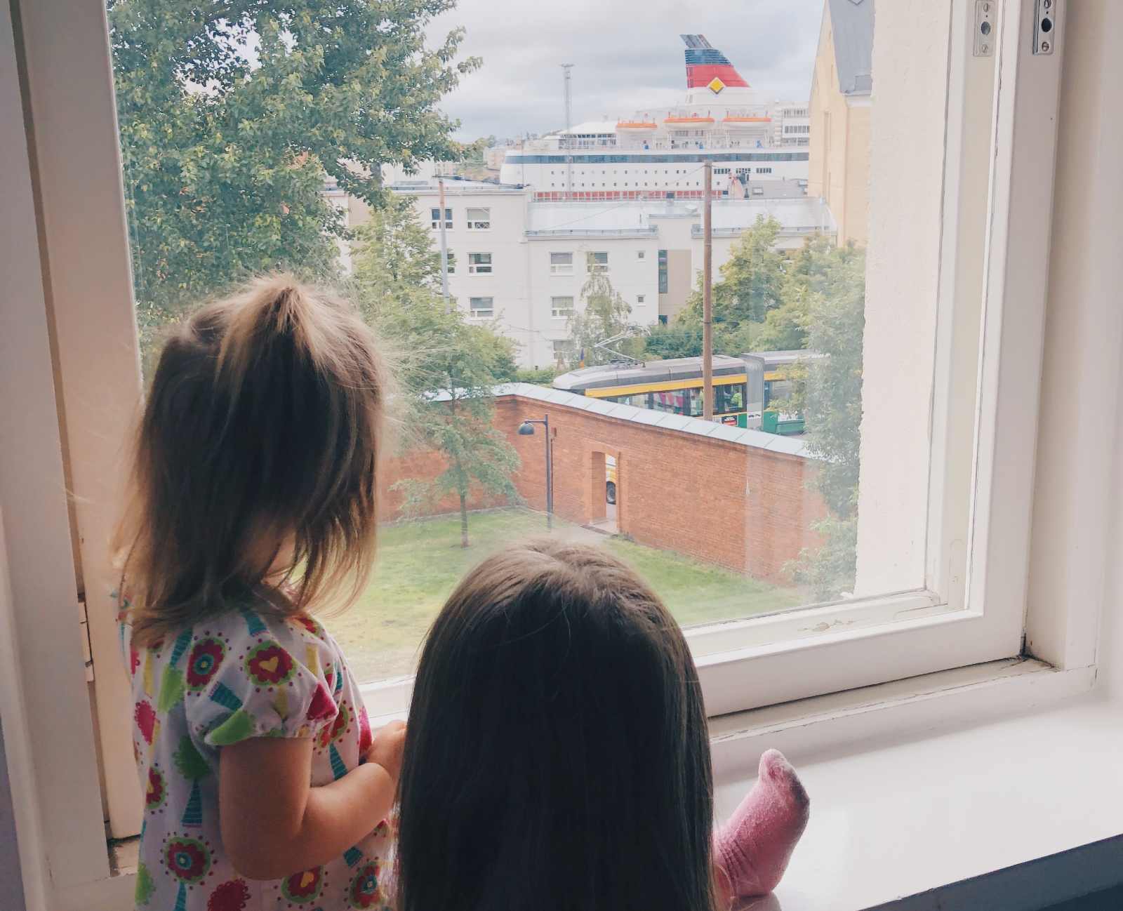 Kids looking at a ferry going on a day trip in hotel room window in Helsinki